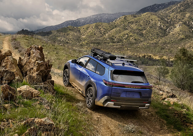 2026 Subaru EV SUV driving up a steep, rocky incline.
